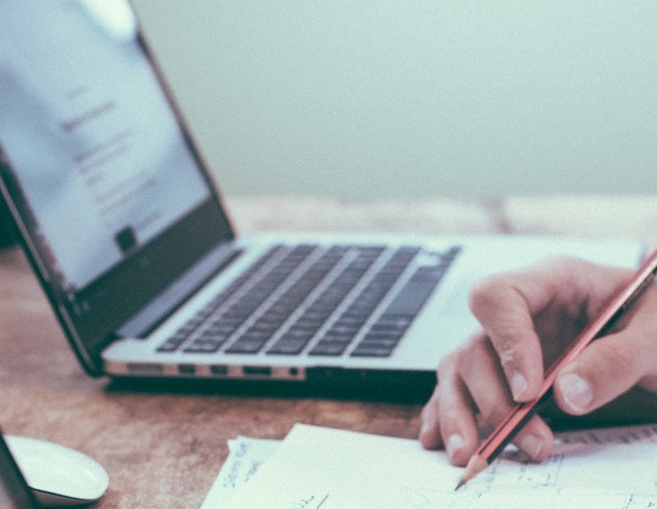 person holding a pencil next to an open laptop/