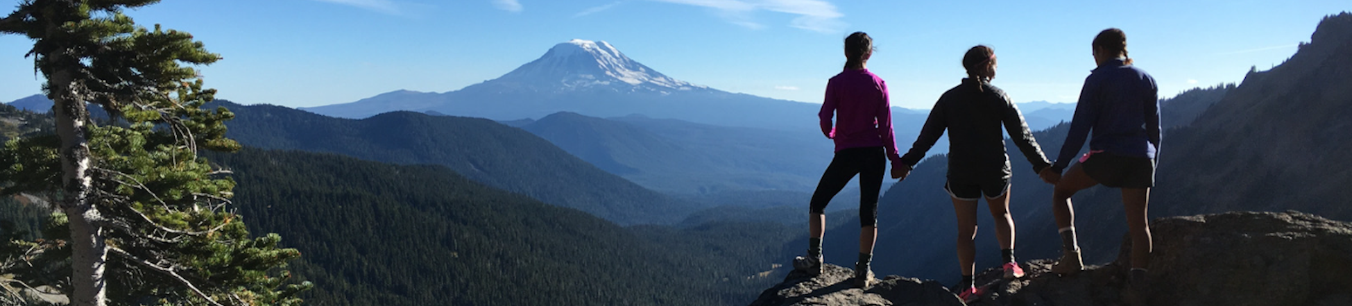 three students standing on a ridege looking towards a mountain in the distance