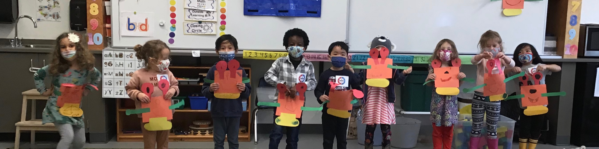 youngs students standing in a row holding up paper art projects