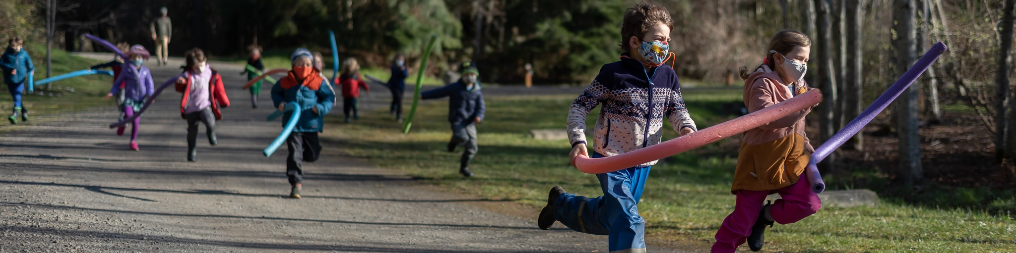 young masked student running with pool noodles