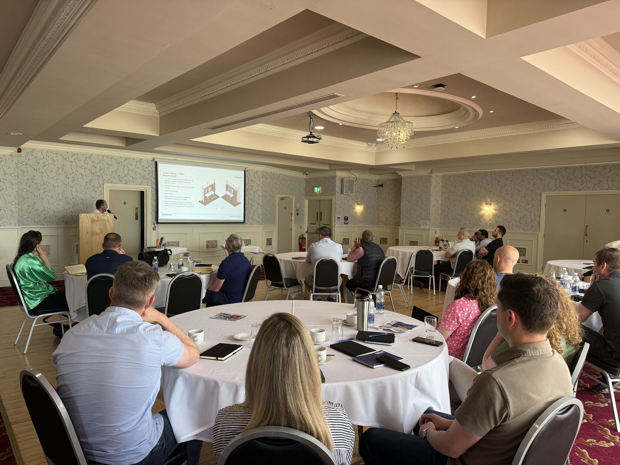 People sitting at round tables looking at a presentation on a screen