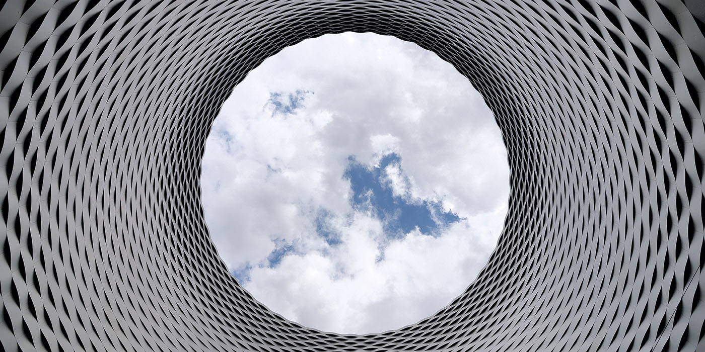 Photo of a modern building forming a ring, with the camera looking upwards through the ring to the sky