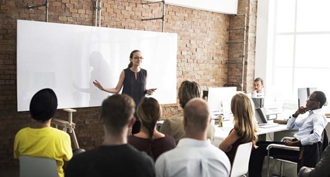 Image of a woman standing in front of a group of people and a white board 