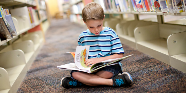 Boy reading a book between two library shelves