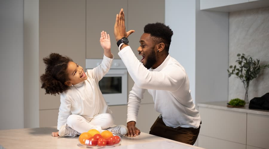 A black dad high fives his daughter on the kitchen island