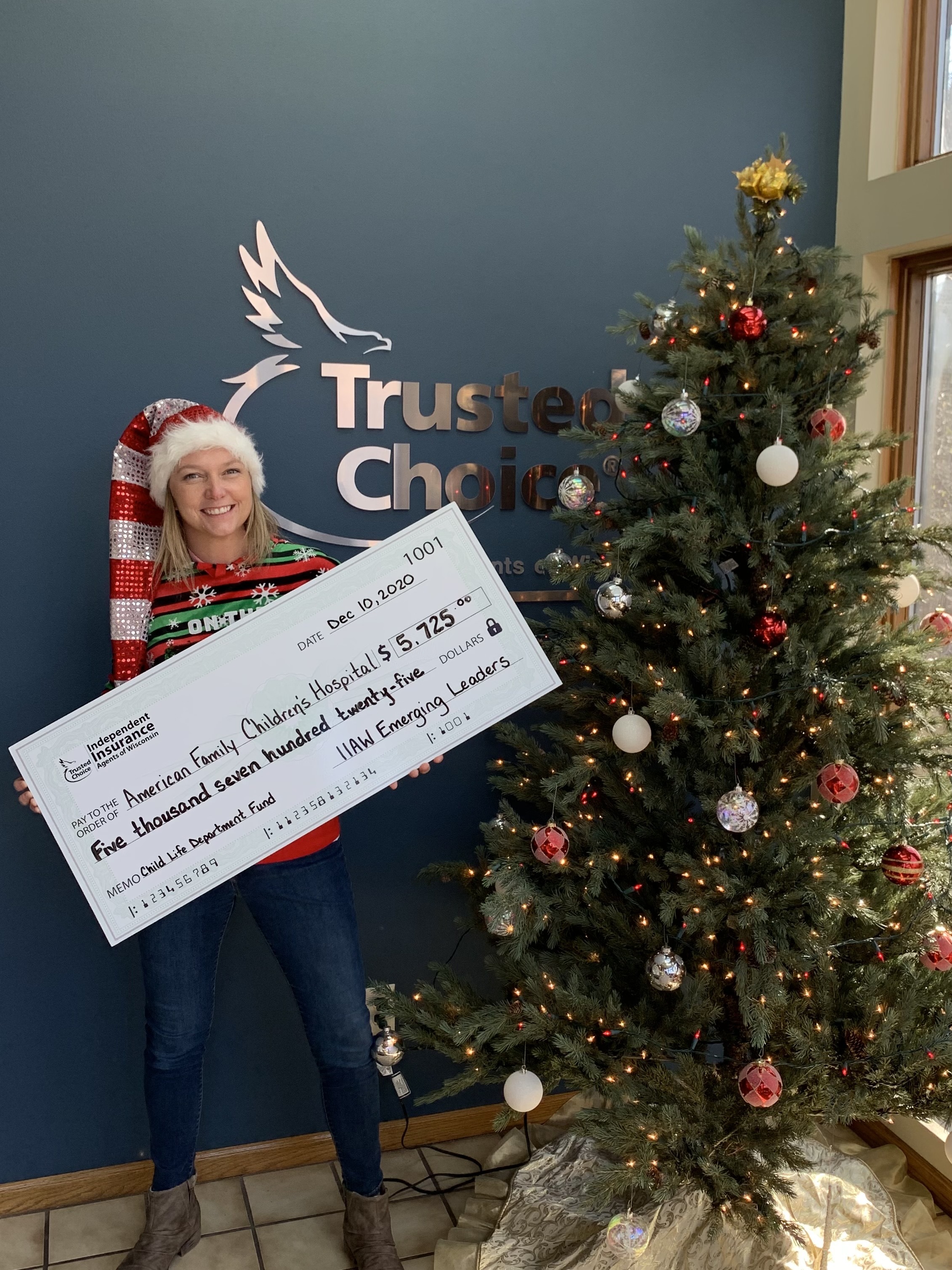 Mallory Cornell, IIAW VP, with $5,725 check for American Family Children's Hospital Check in front of Christmas Tree