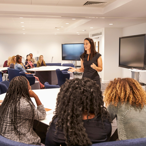 Female professor facilitating a classroom discussion with a large group of students.