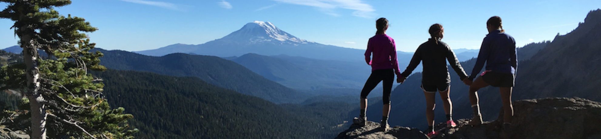 three students standing on a ridege looking towards a mountain in the distance