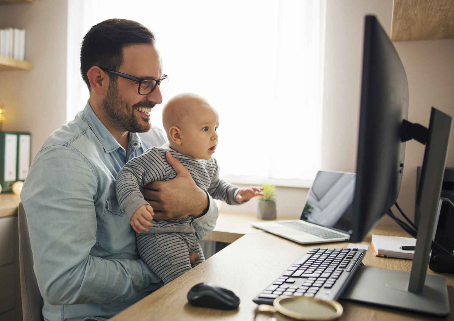 Father holding infant son and looking at computer screen