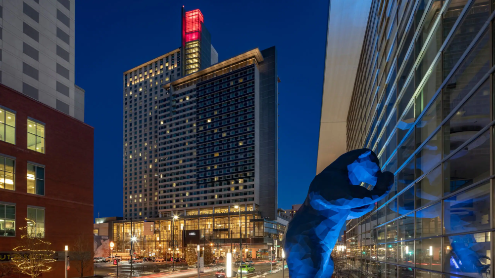 A photograph of the Hyatt Regency Denver in the distance with the Convention Center I See What You Mean statue, also known as the Big Blue Bear, in the foreground.