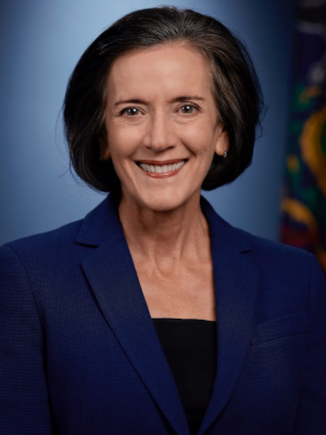 A portrait of Secretary Valeria Arkoosh. She has dark, jaw-length hair, parted to her left and is wearing a dark blue suite jacket.