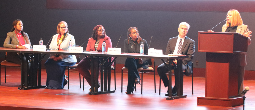 A photograph of Representative Lucy McBath speaking at a podium while the rest of the panelists look on.