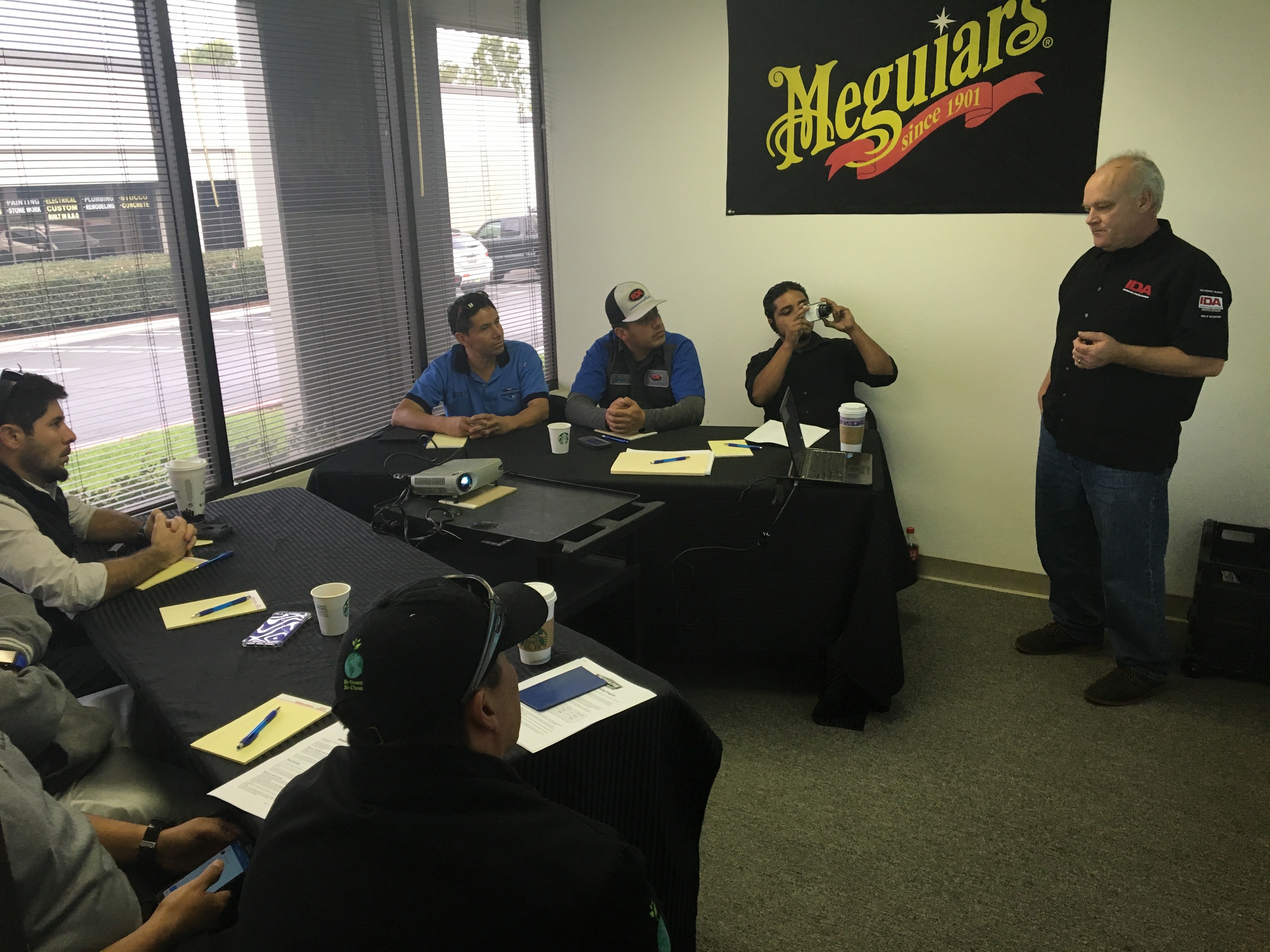 Photo of a room with windows with St. Clair speaking as several detailers sit at tables taking notes.