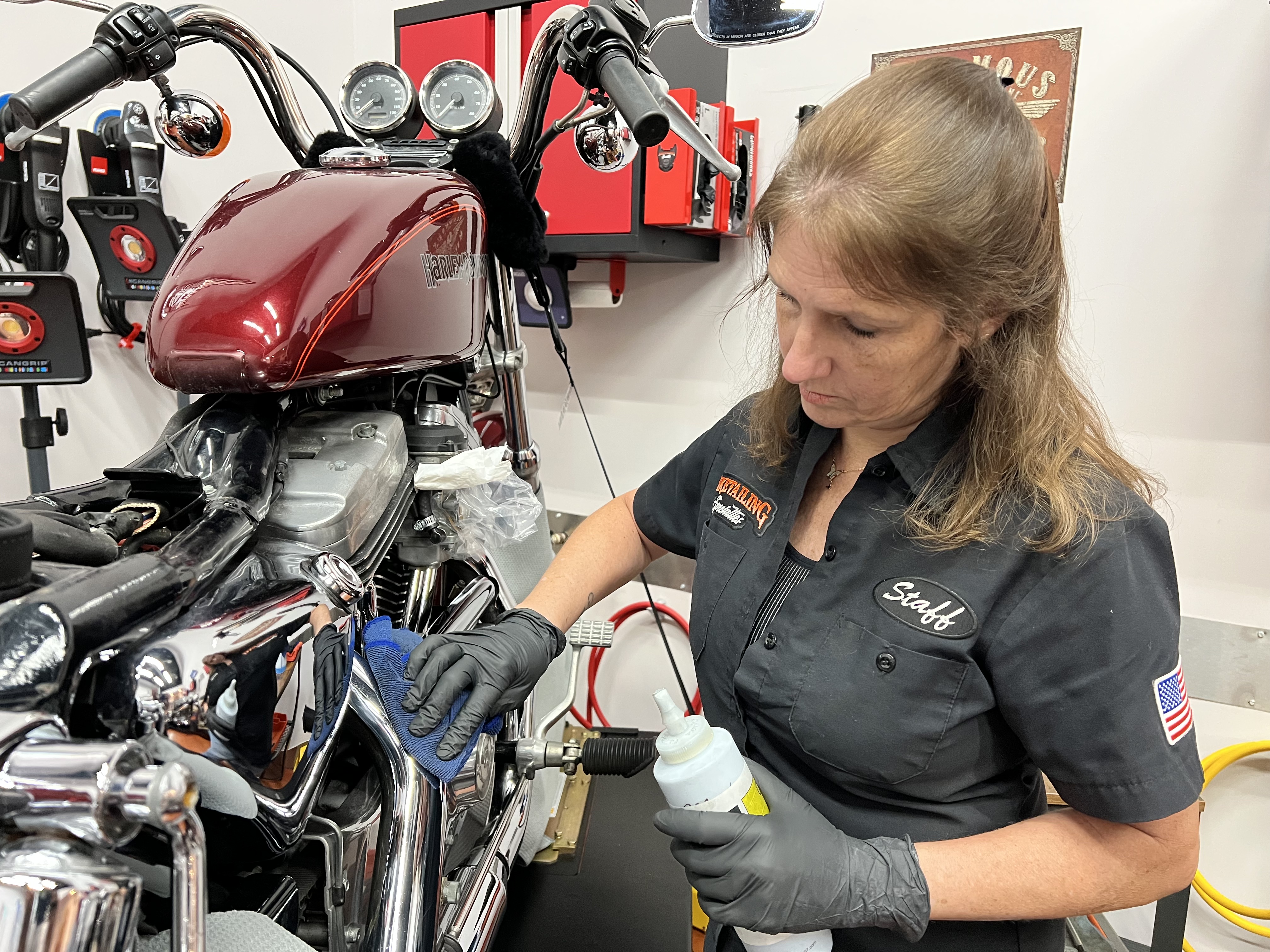 Julie Jimenez wearing gloves, holding a product bottle in her left hand and a rag in her right hand, as she polished the finish on a motorcycle.