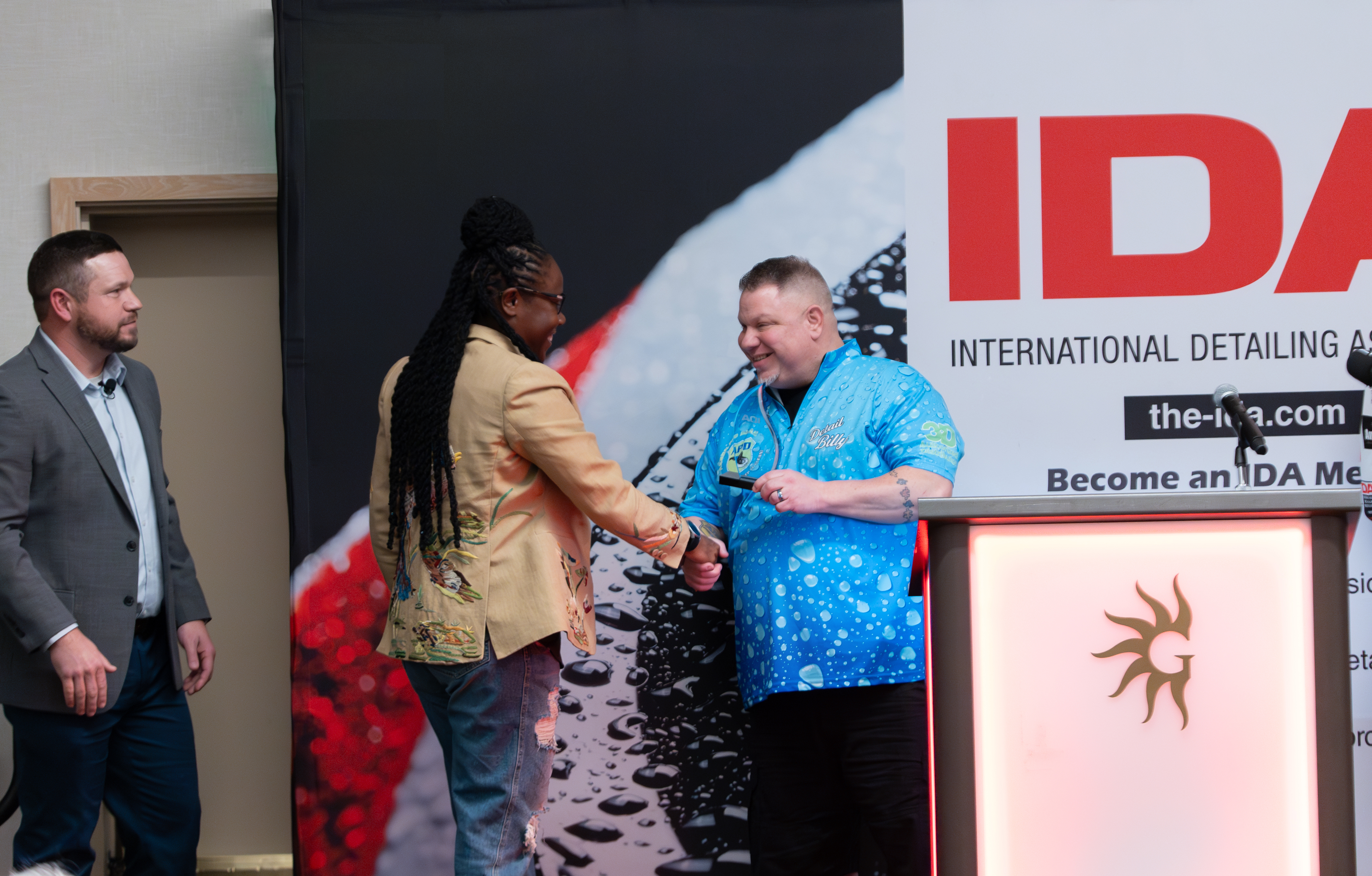 Onika Waldron walking up onto the stage, shaking hands with Chis as she accepts the award from him.