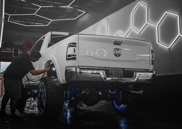 Photo of Steven Thompson holding a light above the tire on a white truck sitting in the shop.