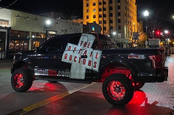 A photo of a black truck sitting outside on the pavement at night.