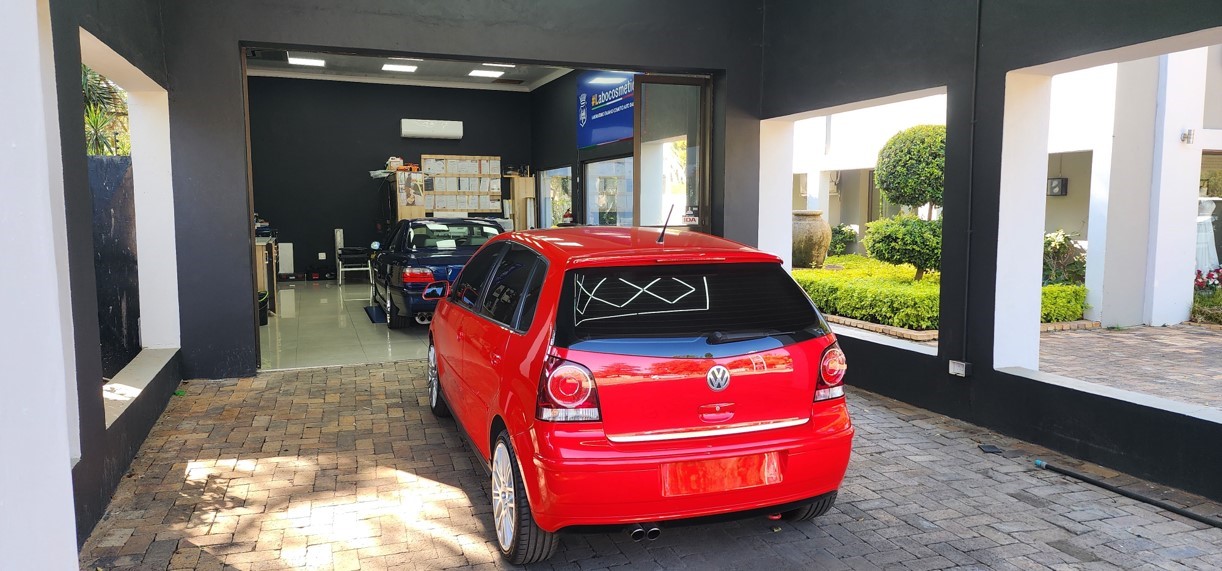 Photo of Hybrid Detailing shop, two large windows look outside, the rear end of a red car can be seen inside the garage