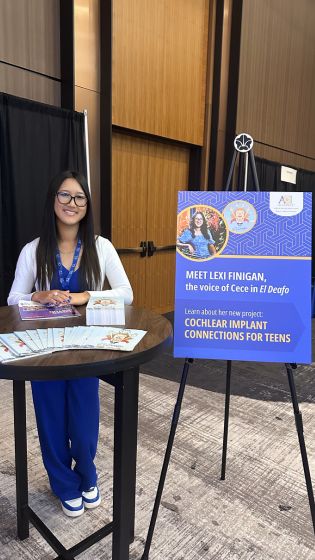 Lexi Finigan standing behind her table at the CI2025 conference